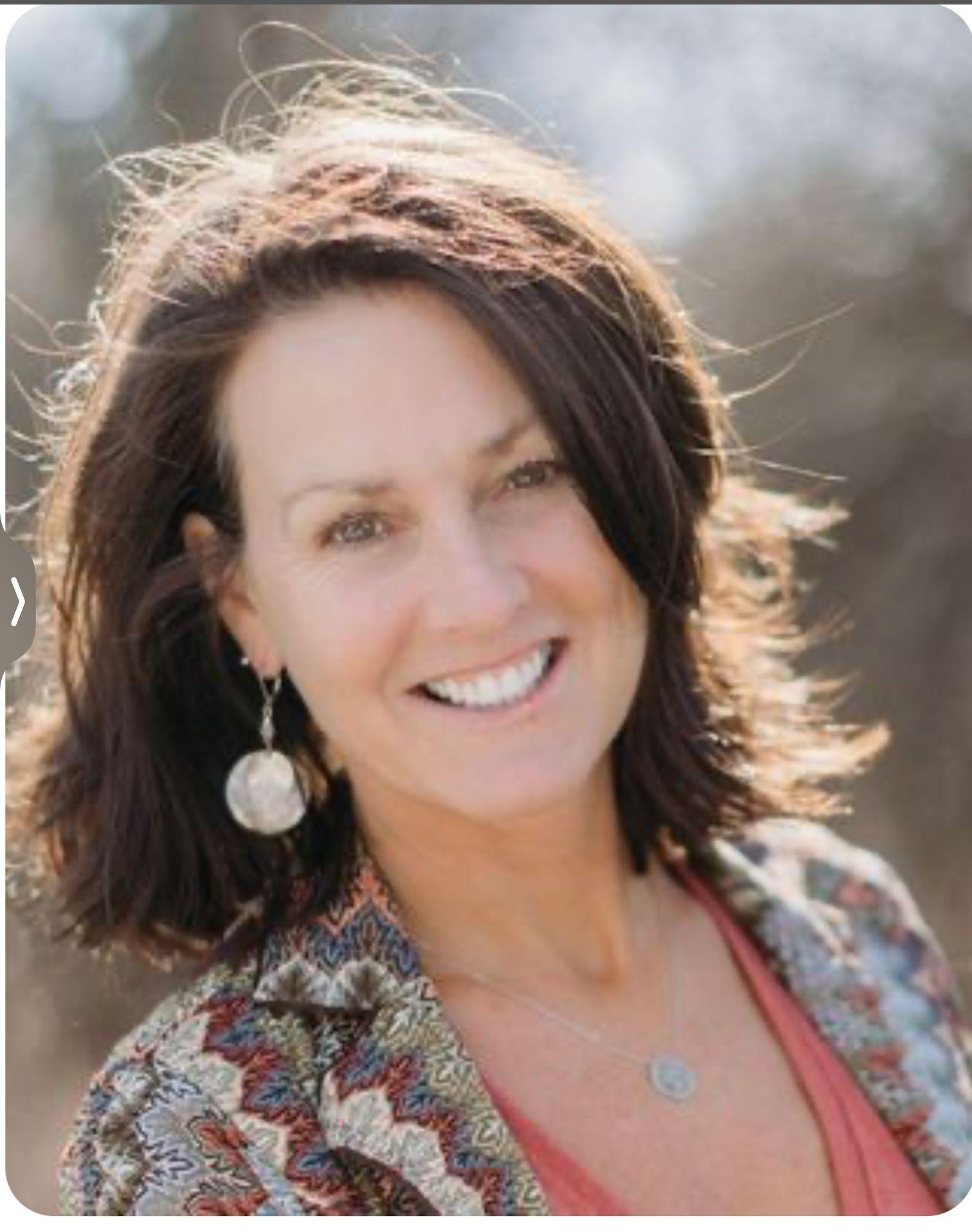 Close-up of a person with shoulder-length brown hair wearing a colorful patterned jacket and coral top.